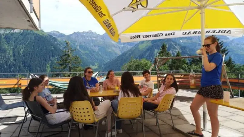 Gruppenunterkunft Adrenalin Backpackers Hotel Braunwald - Leute sitzen unter einem Schirm am Tisch.