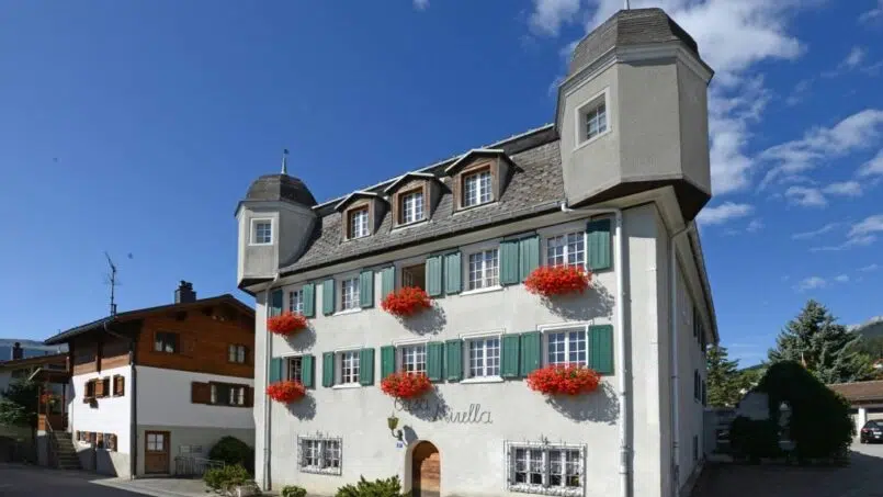 Gruppenunterkunft Casa Mirella in Breil/Brigels - Weißes Gebäude mit roten Blumen in den Fenstern