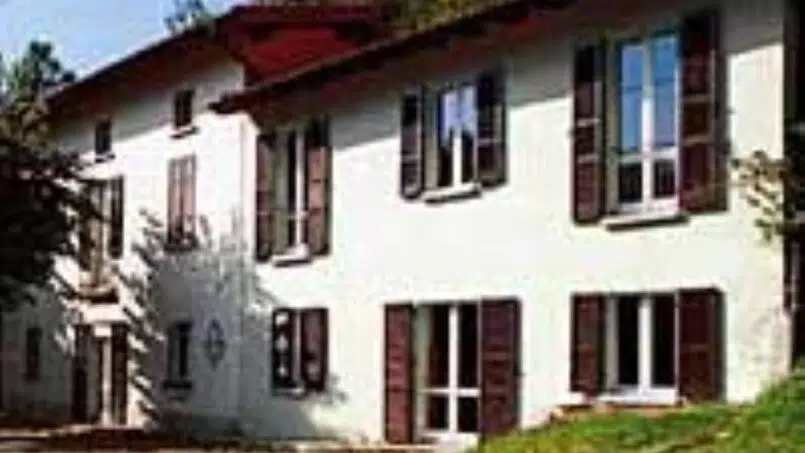 Gruppenunterkunft Centro Scaut la Piana Aget in Somazzo - Weißes Haus mit braunen Fensterläden auf einem Hügel