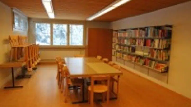 Gruppenunterkunft-Haus-Christkath-Jugendhaus-Giswil-Raum-mit-Tisch-Stühlen-und-Bücherregalen