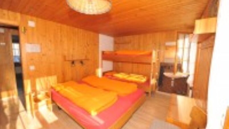 Gruppenunterkunft-Clubhaus-Baumen-SAC-Oberaargau-Grindelwald-Zimmer-mit-Etagenbetten-und-orangefarbenen-Bettwäsche
