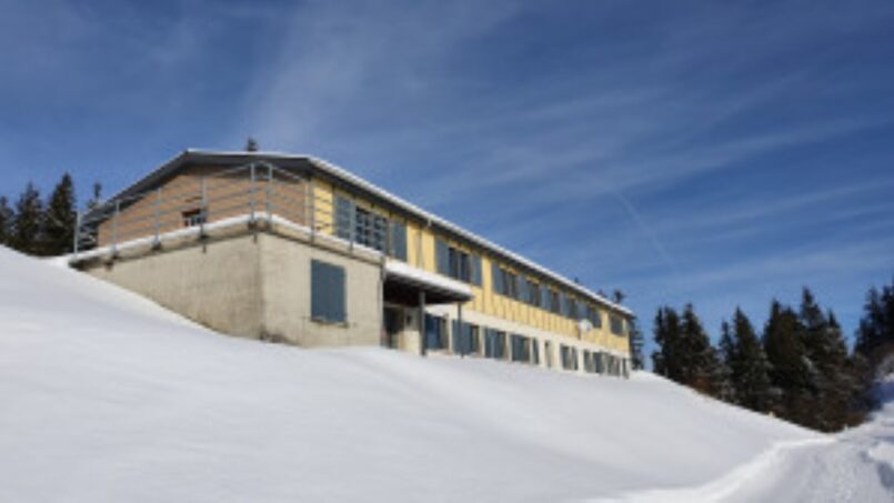 Gruppenunterkunft-Ferienheim-Schrattenblick-Marbach-gelbes-Gebäude-auf-schneebedecktem-Hügel