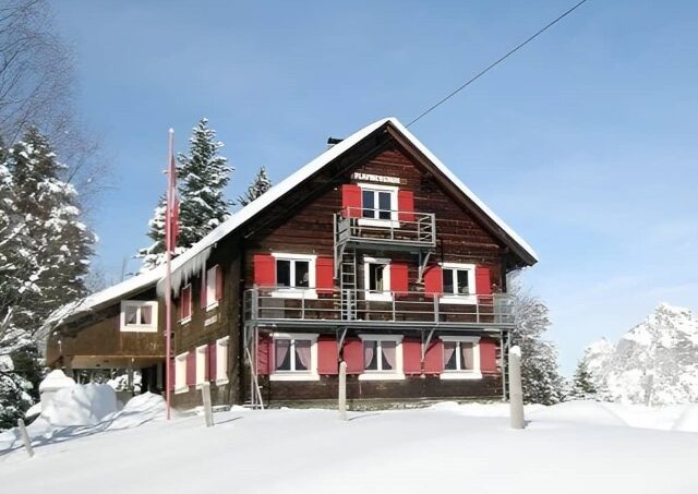 Gruppenunterkunft-Haus-Flamberghuis-Blüemlisegg-Stoos-Holzhaus-mit-roten-Läden-im-Schnee