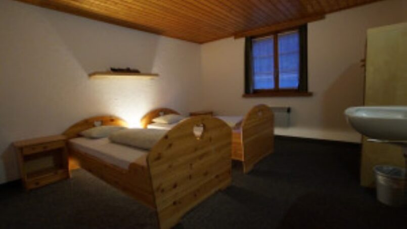 Kleines Schlafzimmer mit zwei Betten und Waschbecken im Gruppenhaus-Hotel Rheinquelle in Sedrun - Gruppenunterkunft