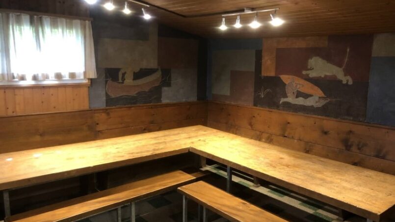 Holzbänke im Zimmer der Gruppenunterkunft Hütte Vogelweide in Pratteln mit Gemälde an der Wand