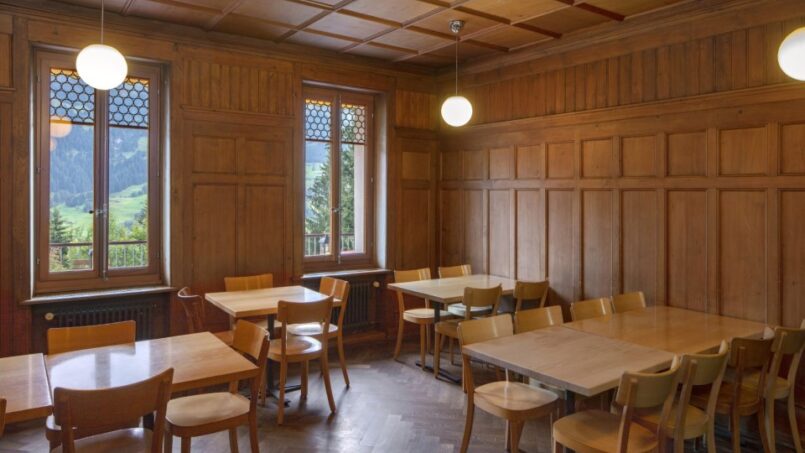 Holzvertäfeltes Zimmer mit Tischen und Stühlen in der Jugendherberge Grindelwald