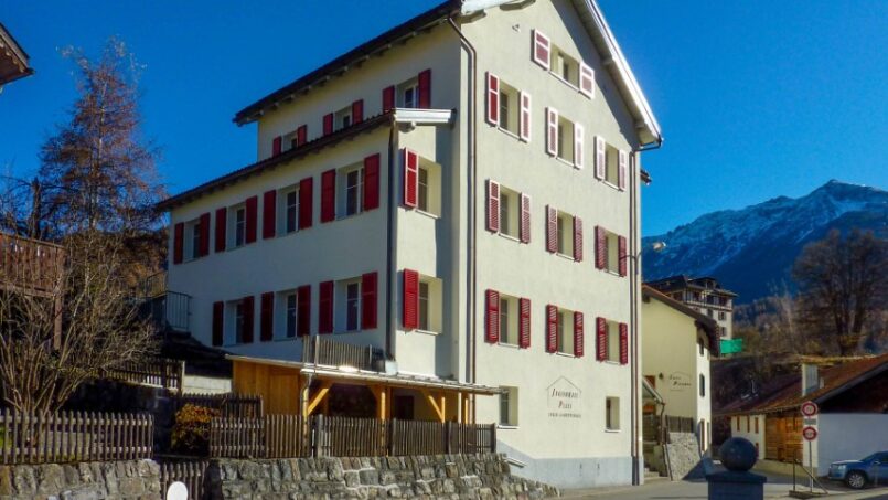 Gruppenunterkunft-Jugendhaus-Plazi-Bergün-weisses-Gebäude-mit-roten-Fensterläden-vor-Bergkulisse