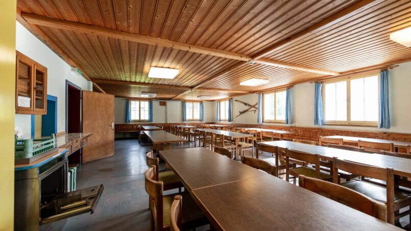 Leerer Speisesaal mit Holztischen und -stühlen in der Gruppenunterkunft Casa Clau in Rueun