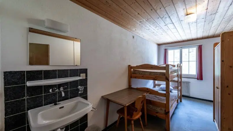 Kleines Zimmer mit Etagenbetten und Waschbecken im Gruppenhaus Casa Clau in Rueun - Gruppenunterkunft