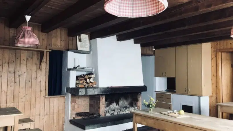 Gruppenhaus Pfadiheim Parmort Küche mit Holztischen und Stühlen sowie Kamin in Madris-Vermol