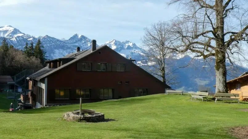 Gruppenunterkunft Jugendhaus Ramsern in Beatenberg - rotes Gebäude mit grünem Hof und Bergen im Hintergrund