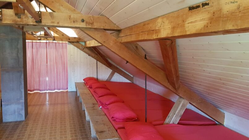 Gruppenhaus Waldhaus Ischlag in Menziken - Dachzimmer mit Holzbalken und roten Kissen